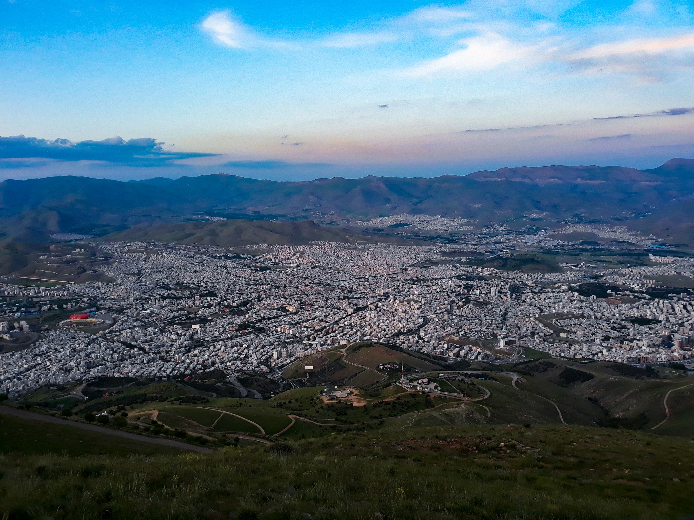 The city of Sanandaj nestled among the mountains at dusk, seen from Awyar